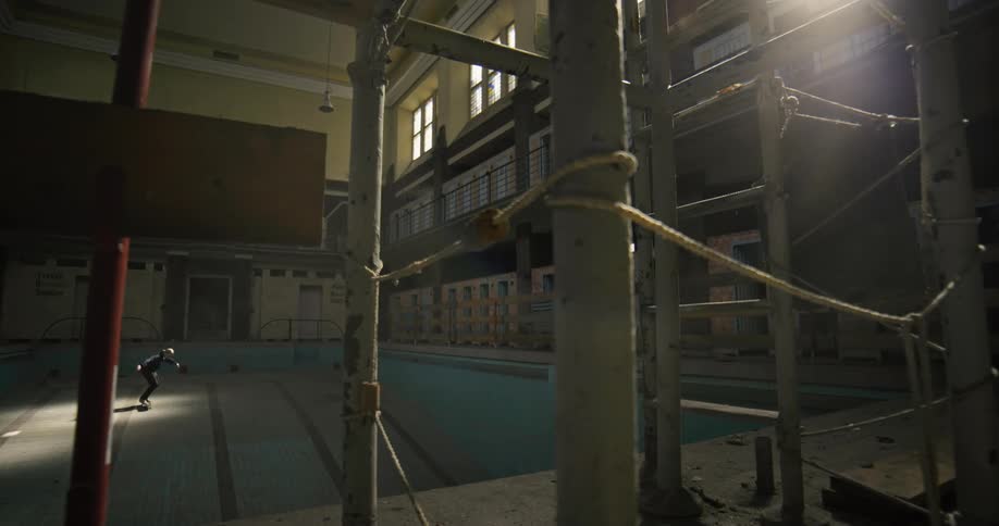 Skateboarder attempts jump trick in bottom of empty indoor swimming pool