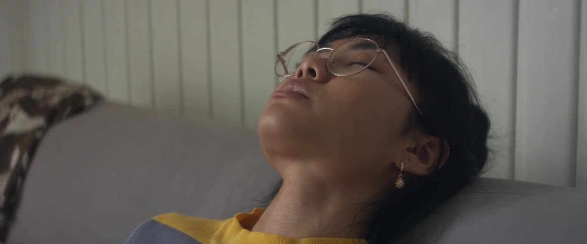 Girl with glasses earrings and stripped tshirt sitting on bed uses smarphone tilting his bed
