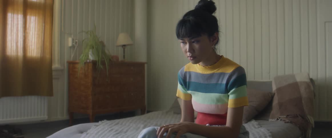 Asian teenager girl sitting at the bed and using her smartphone in a introspective way alone at her room