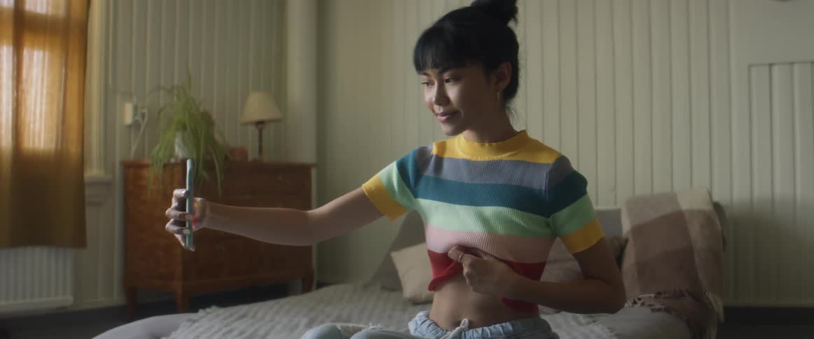 A woman lifts her shirt to take a photo of her stomach with her smartphone