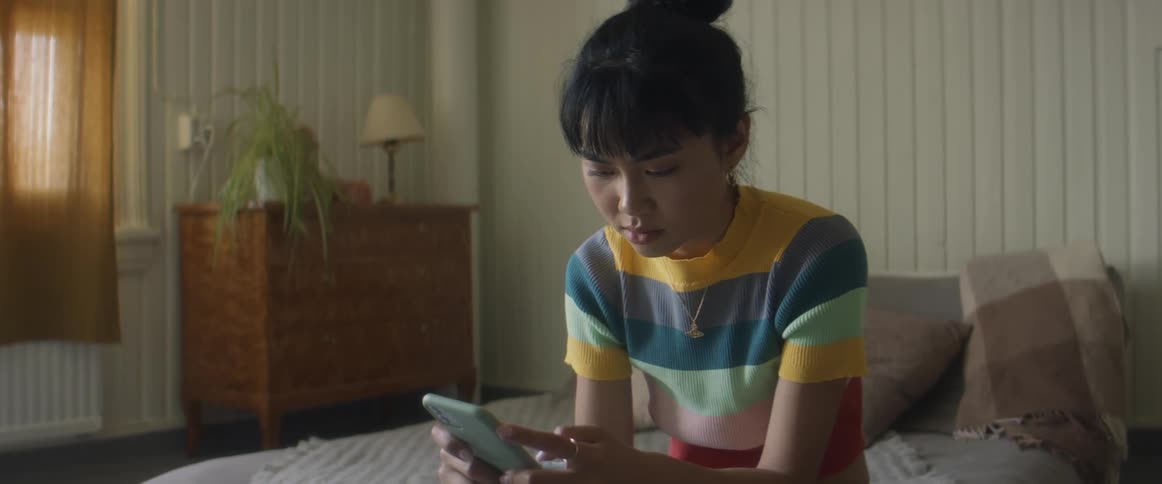 Girl with glasses earrings and stripped tshirt sitting on bed uses smarphone