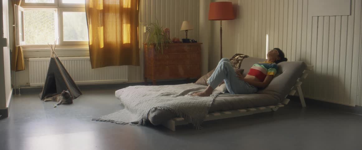 Girl with stripped shirt and ripped jeans sits on bed using smartphone in bedroom