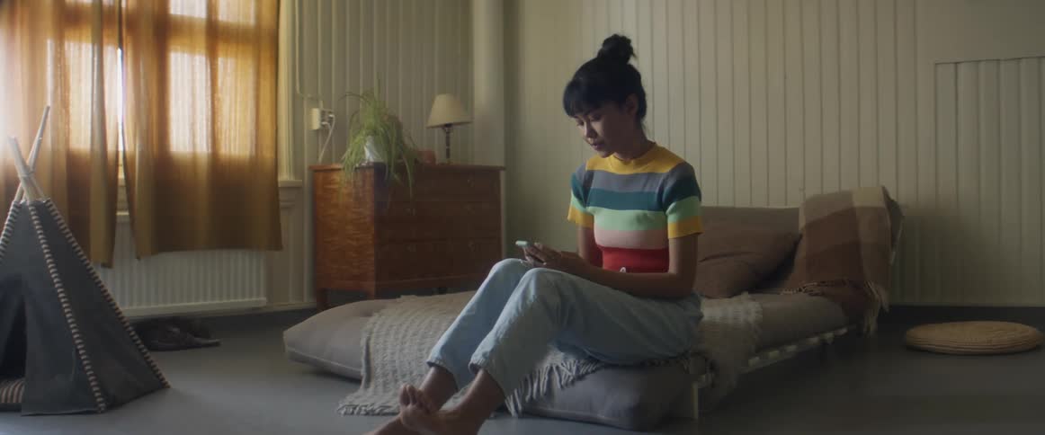 A woman is sitting indoors and looking at a cell phone