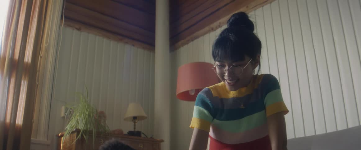 Girl with glasses stripped shirt and ripped jeans pets gray cat sitting on bed in bedroom