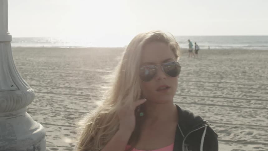 A blonde woman talks on her phone at the beach