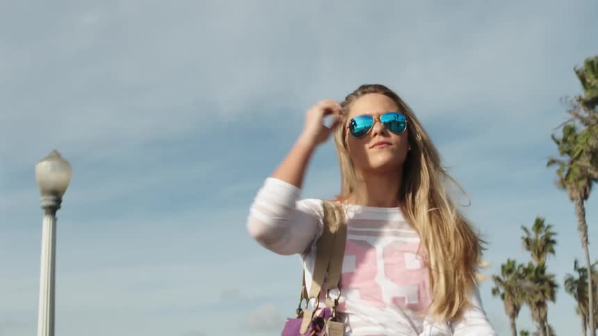 A woman brushing back her hair and removing her sunglasses while walking