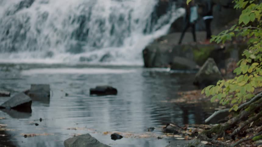 A couple stands on a rock ledge as the waterfall flows behind them