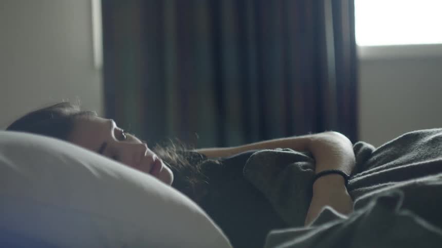 A woman is lying in bed then she sits up and looks around