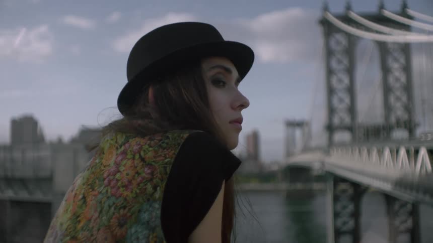 A woman wearing a hat looks over by the water on a cloudy day