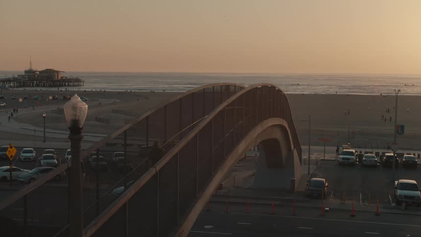 Vehicles pass under a pedestrian bridge that leads to a beach on the coast