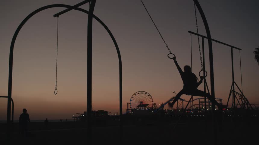 A young women swings across monkey bars on the playground of Santa Monica
