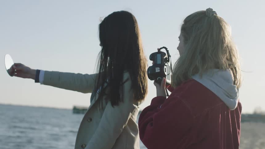A photographer holding her camera gives direction to a model holding a mirror in her outstretched arm