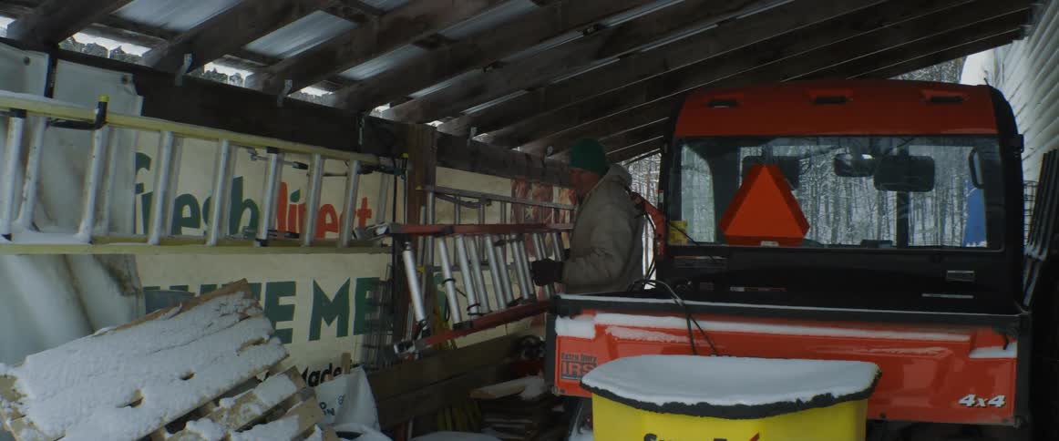A man takes a ladder off a wall in a shed and carries it outside
