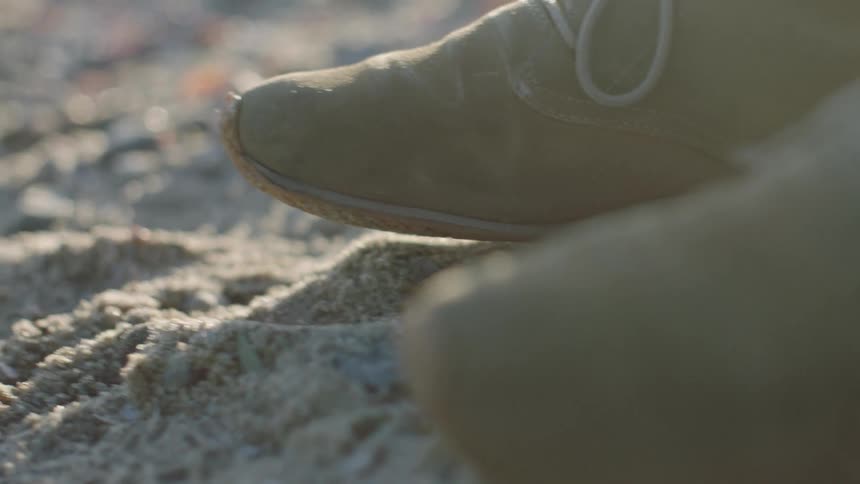 Grey shoes stepping on the sand at the beach during day time
