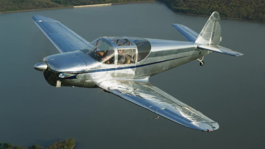 The sun is shining brightly upon a small airplane flying over a forest and lake