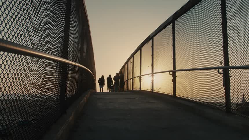 People walk over a bridge at sunset