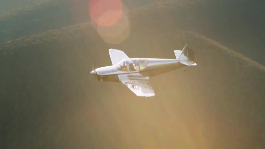 A silver plane is flying over the hills