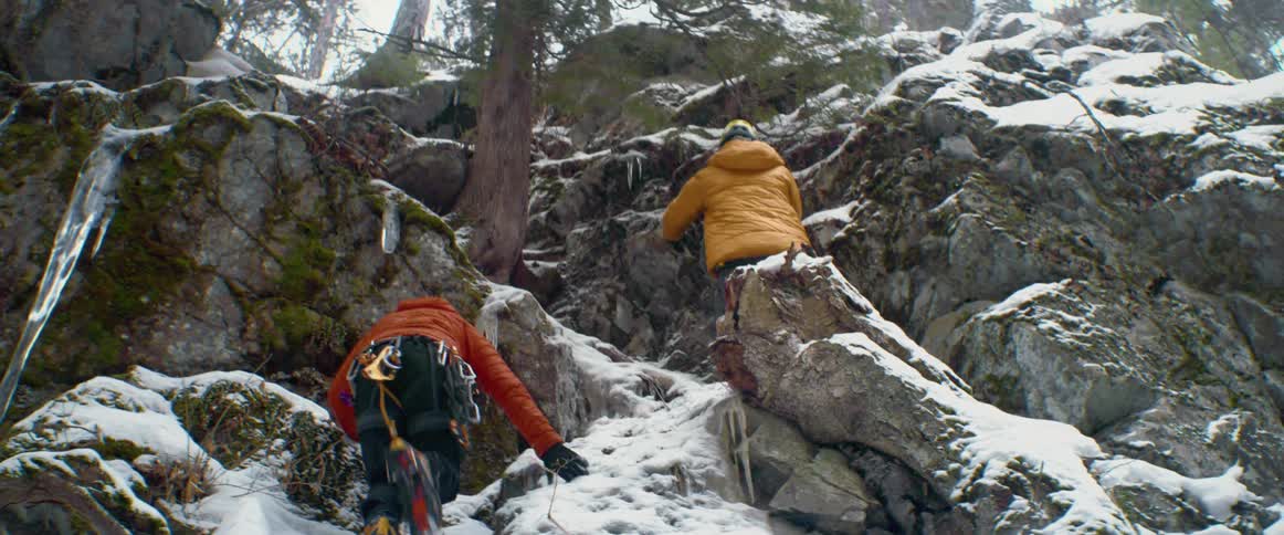 Two rock climbers climb up the snowy rocks