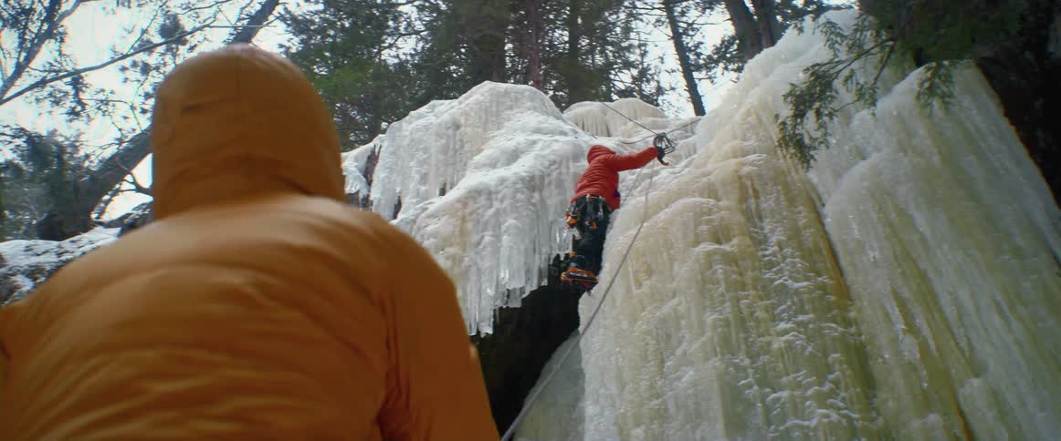 A person holds a rope for another person climbing an ice covered mountain