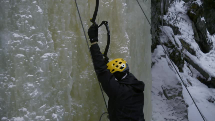 An ice climber uses ice axes and ropes to climb ice on a mountain during the day