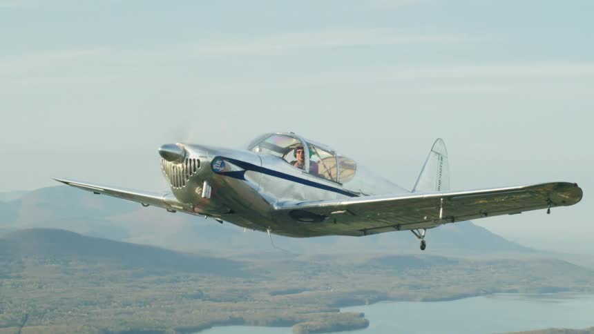 Pilot flies small propeller plane over misty river and forest bordered by mountains