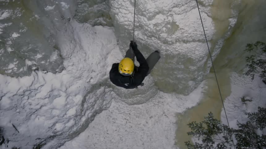 A person uses a rope to climb down a snow covered mountain