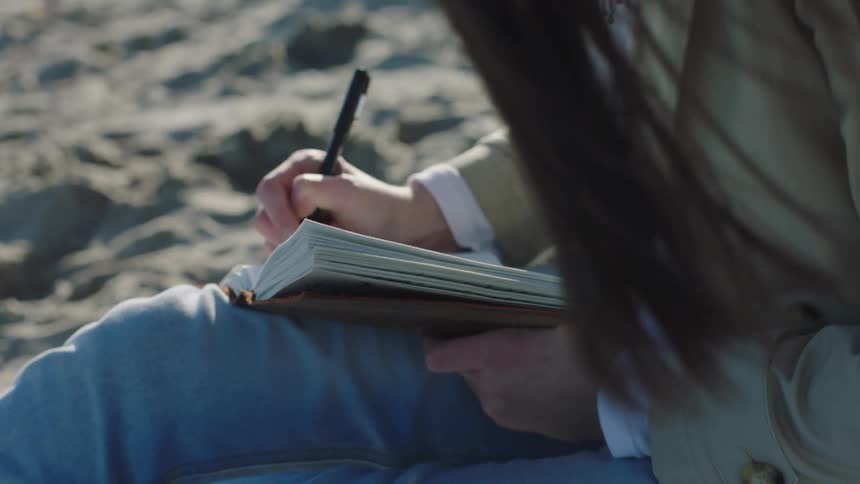 A woman is writing in her notebook on the beach