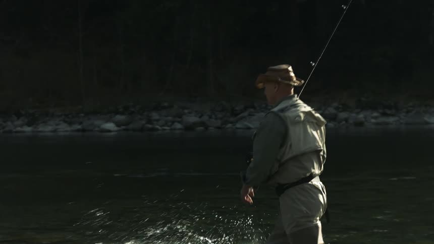 A fisherman wades through a river while holding his fishing rod