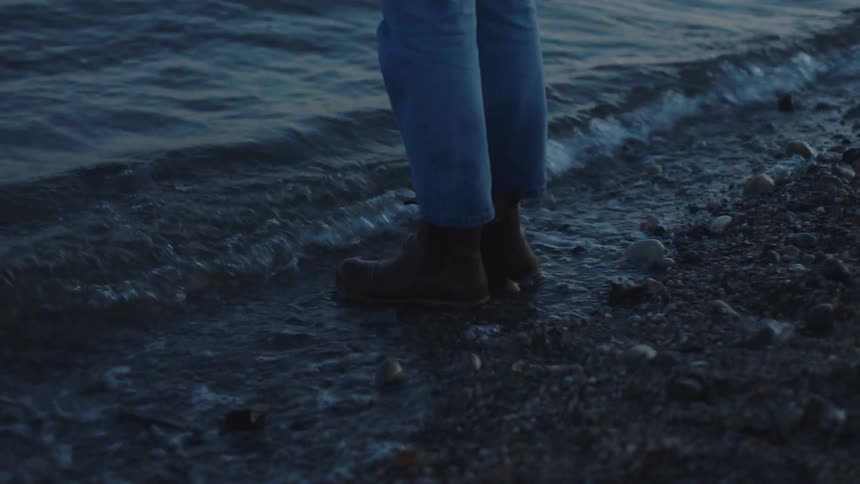 A person stands by the water with a lantern