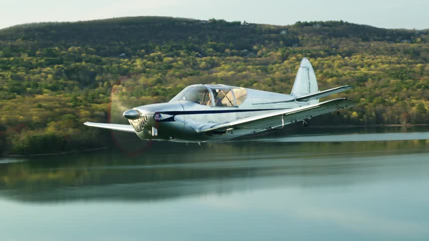 A man is flying a small airplane over a lake near a forest
