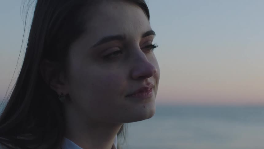 A woman stands on the shore and looks off in to the distance