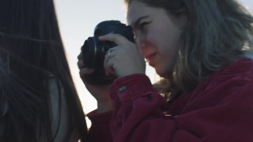 Woman with brown wavy hair and red jacket photographs womans hair as the sun shines