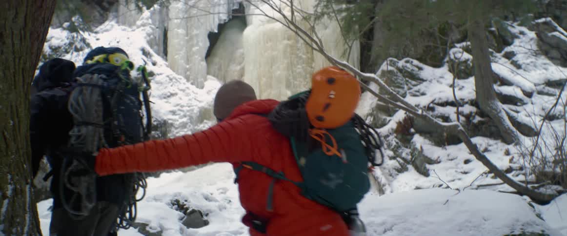 A man grabs onto a tree for support as he and two other men hike through a snow covered forest