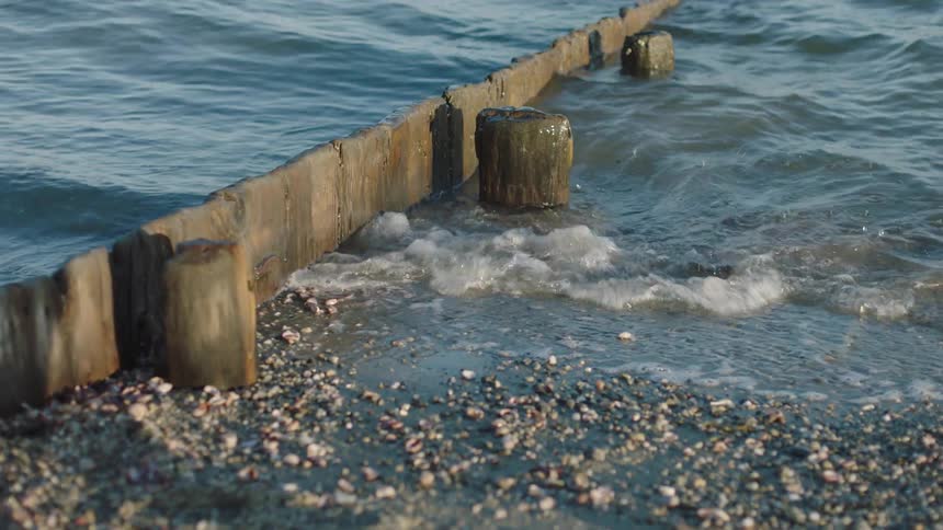 Waves splash against wooden pylons and panels near and on shore
