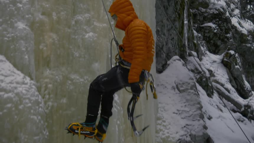 A person uses a rope to climb down an ice covered mountain