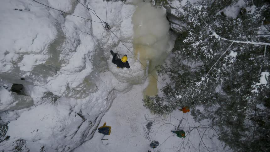 An aerial view of a person on the side of an icy mountain as they climb