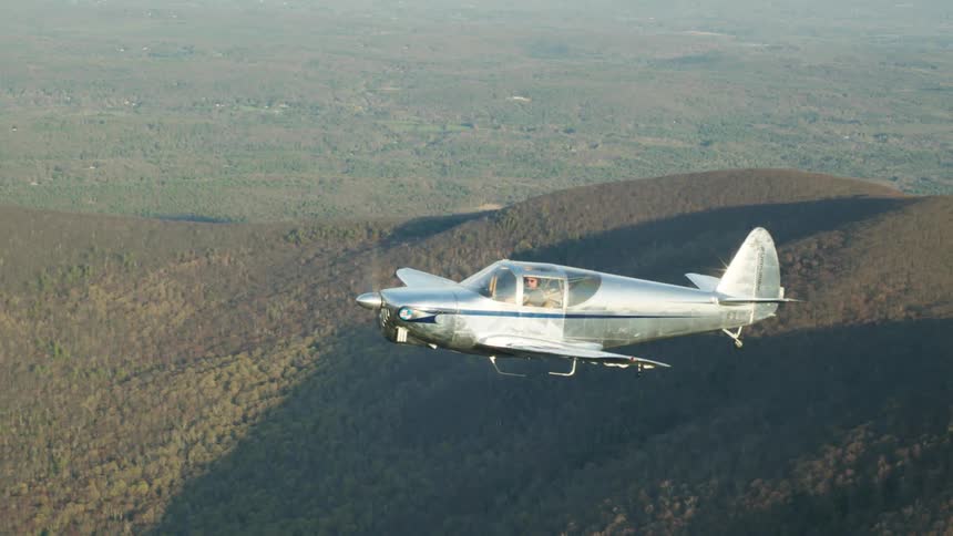 A man is flying a small airplane over forested mountains