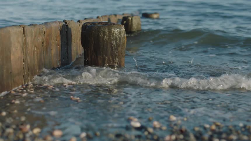 Waves splash against post standing near a low wooden wall leading toward the beach