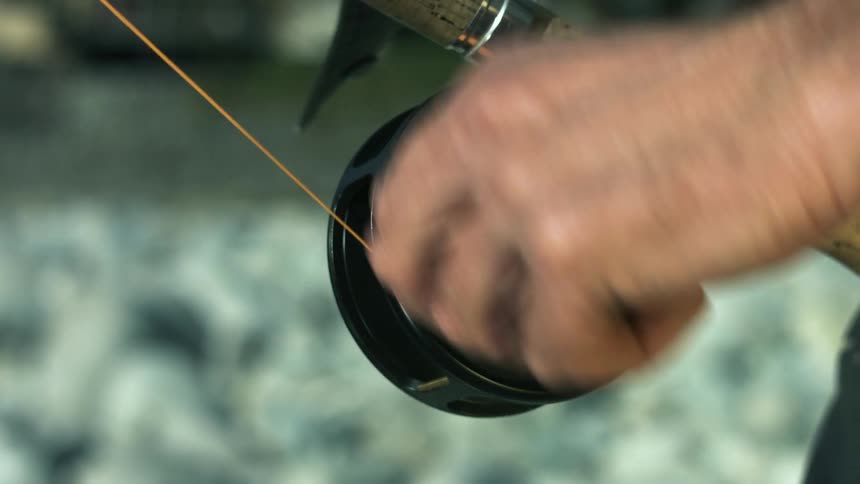 Man winds fishing line by hand cranking fishing reel attached to bottom of fishing pole