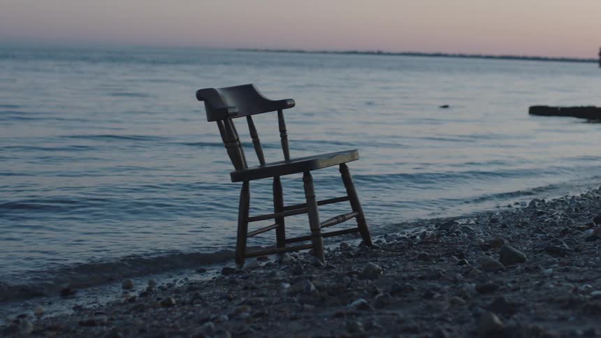 A chair sits on the shore as waves roll in