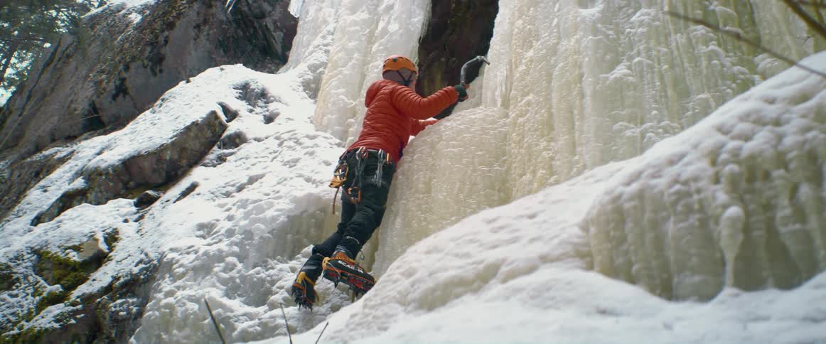 A human puts ice picks in the side of a mountain as they climb up it