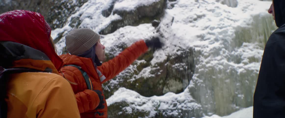 A group of people stand at the bottom of a snowy mountain and plan how they will climb up it
