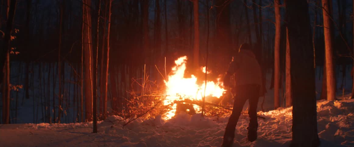 A man is throwing branches into a bonfire