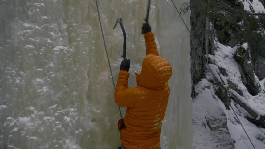 An ice climber reaches up with his axes then checks the ropes