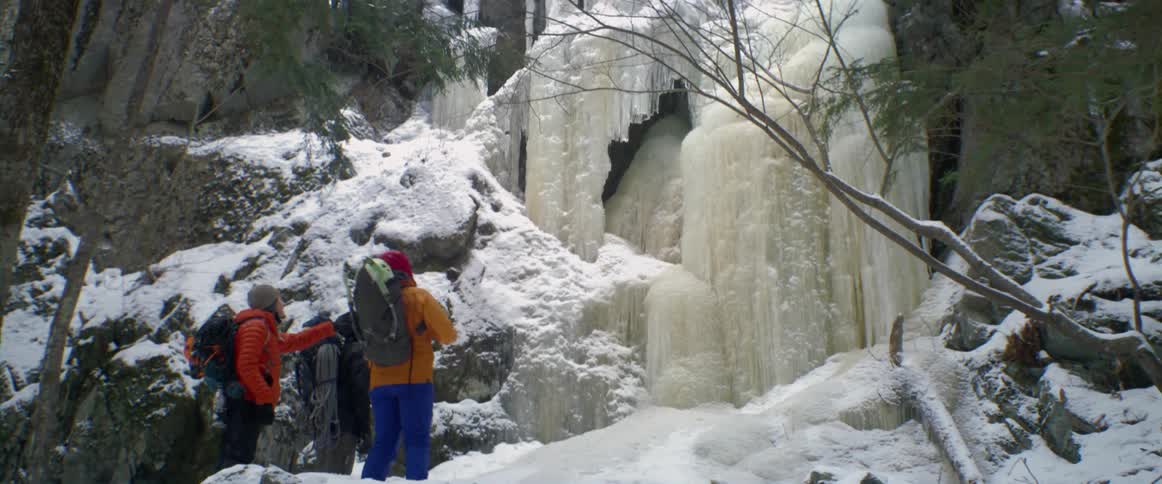 A group of three hikers stops at the base of a frozen cliff