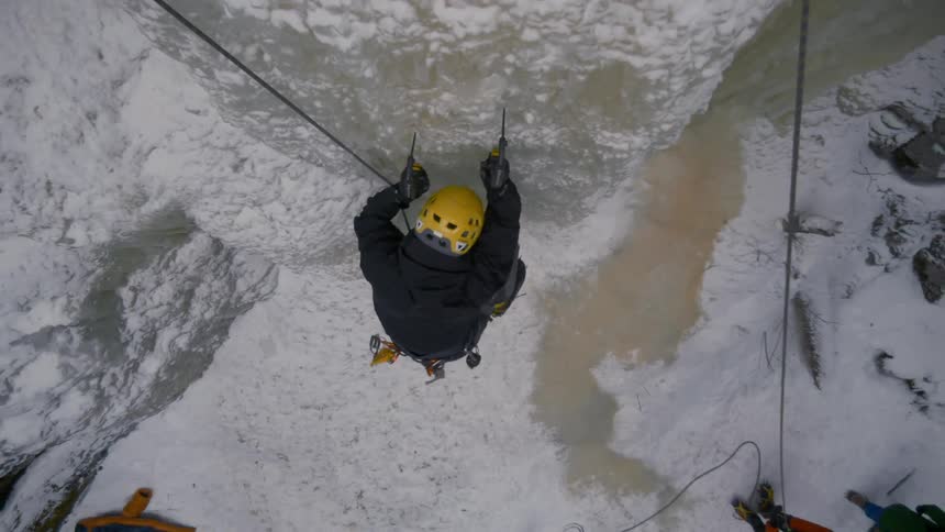 An ice climber uses axes to climb a sheer ice cliff
