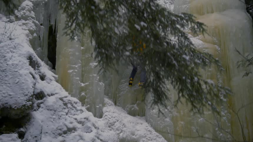 A person putting an ice pick in the side of the mountain as they climb up