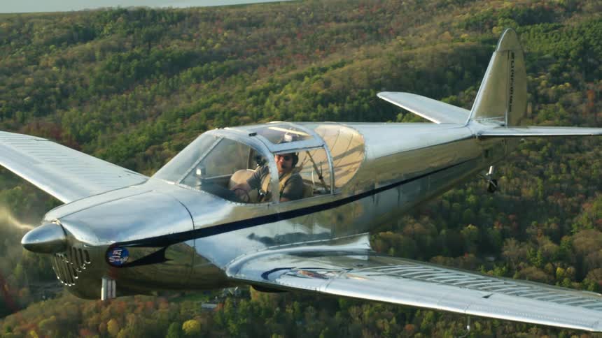 A man is flying a small airplane over a forest