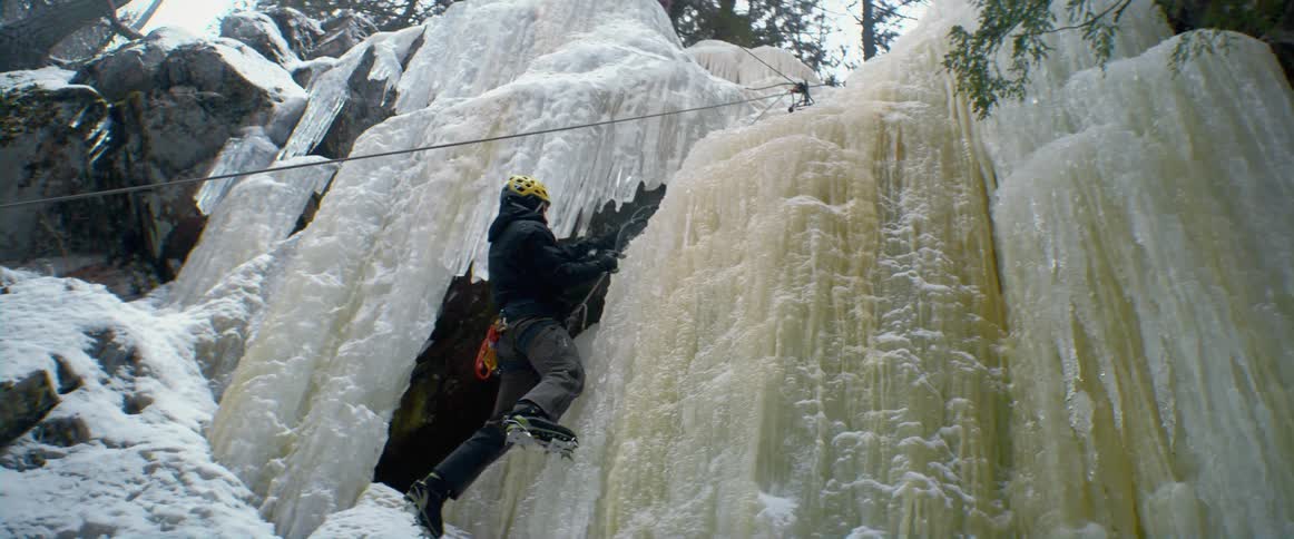 A person puts ice picks on ice on the side of a mountain as they climb up it