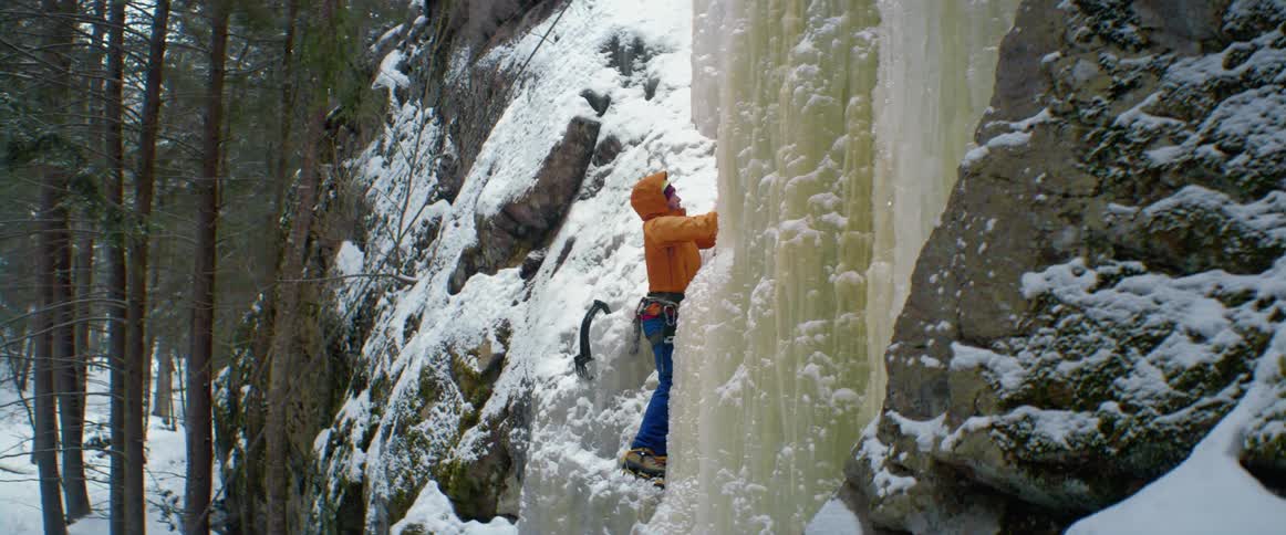 Ice climber uses an ice blade to climb up the ice on the rocks